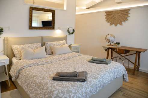 Immagine della camera da letto con letto con coperte, un scrittoio a destra e uno specchio appeso sopra la testiera del letto