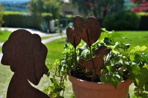 Immagine con una pianta in vaso, delle decorazioni in metallo a forma di cuore e il giardino sullo sfondo